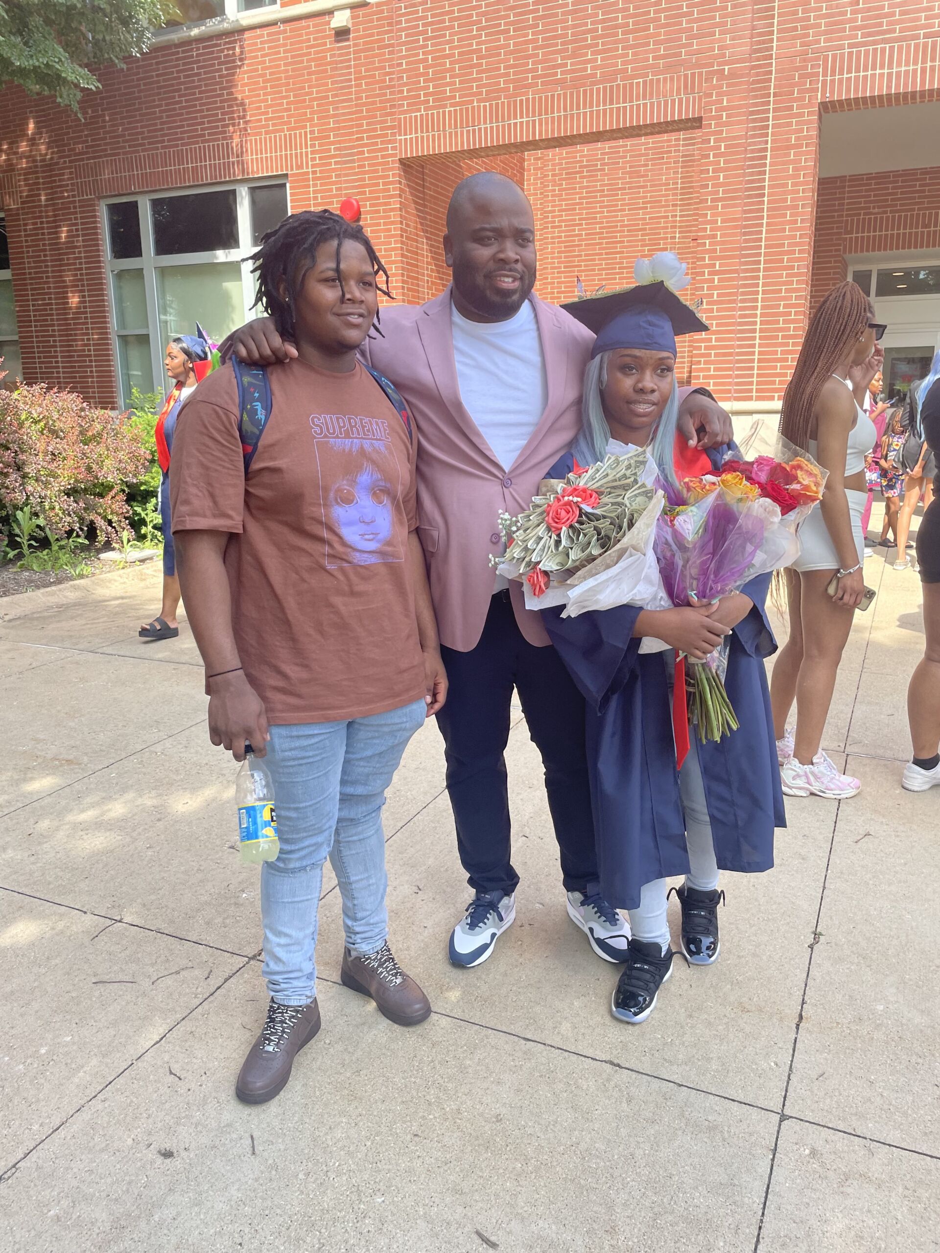 Cleaves standing with two young students, one of whom is in graduation robes. They are all smiling for a photo outside.