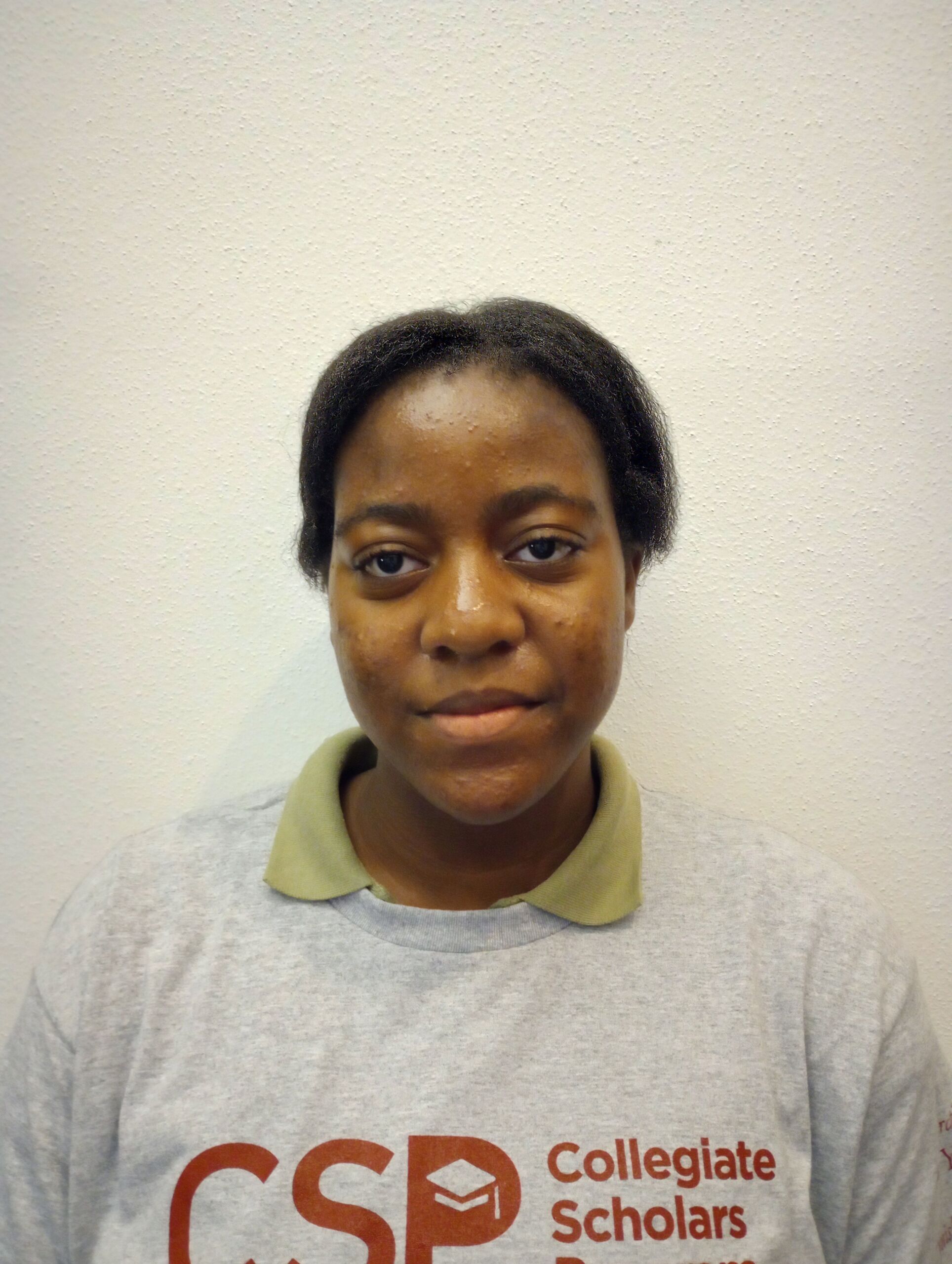 A headshot of Vanelle, a Baker College Prep student. She has medium brown skin, dark brown hair tied back into a ponytail, and is wearing a gray Collegiate Scholars Program sweatshirt. She's smiling.