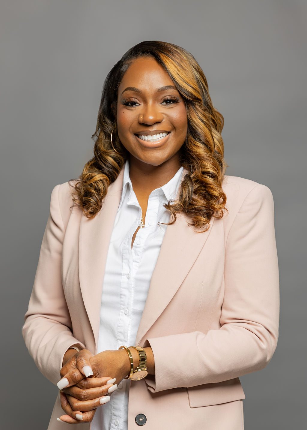 Headshot of Erica Allen. She is a woman with medium-dark brown skin and wavy, shoulder-length dark brown hair with gold-brown highlights. She is smiling and wearing a light pink blazer over a white button up.