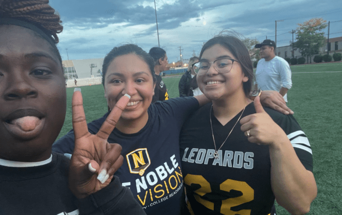 Lizbet Sanchez, a special education teacher at Mansueto High School, poses with two of her students in front of a football field.