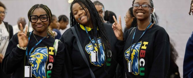 Three Rowe-Clark Math & Science Academy students smile and pose at the HBCU College Fair. They are all wearing matching black sweatshirts with the Rowe-Clark mascot next to the letters HBCU.