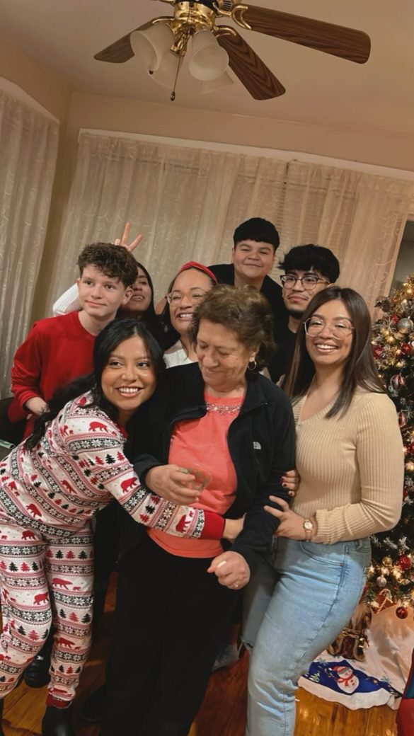 Sanchez and her large family all crowd together for a photo, smiling and standing in front of a Christmas tree.