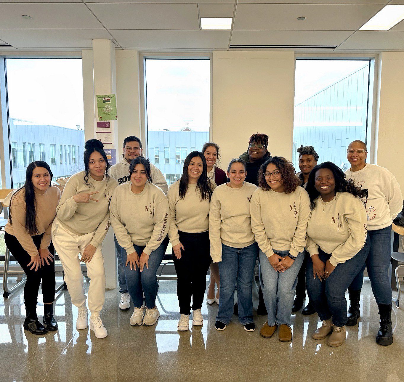 Sanchez poses with many other staff members on the math team at Mansueto. They are all wearing matching white sweatshirts and are standing in a classroom.