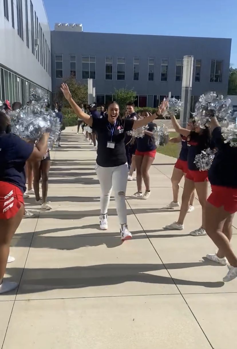 Cora has her hands up in a cheer as she walks through a tunnel of UIC College Prep cheerleaders outside.