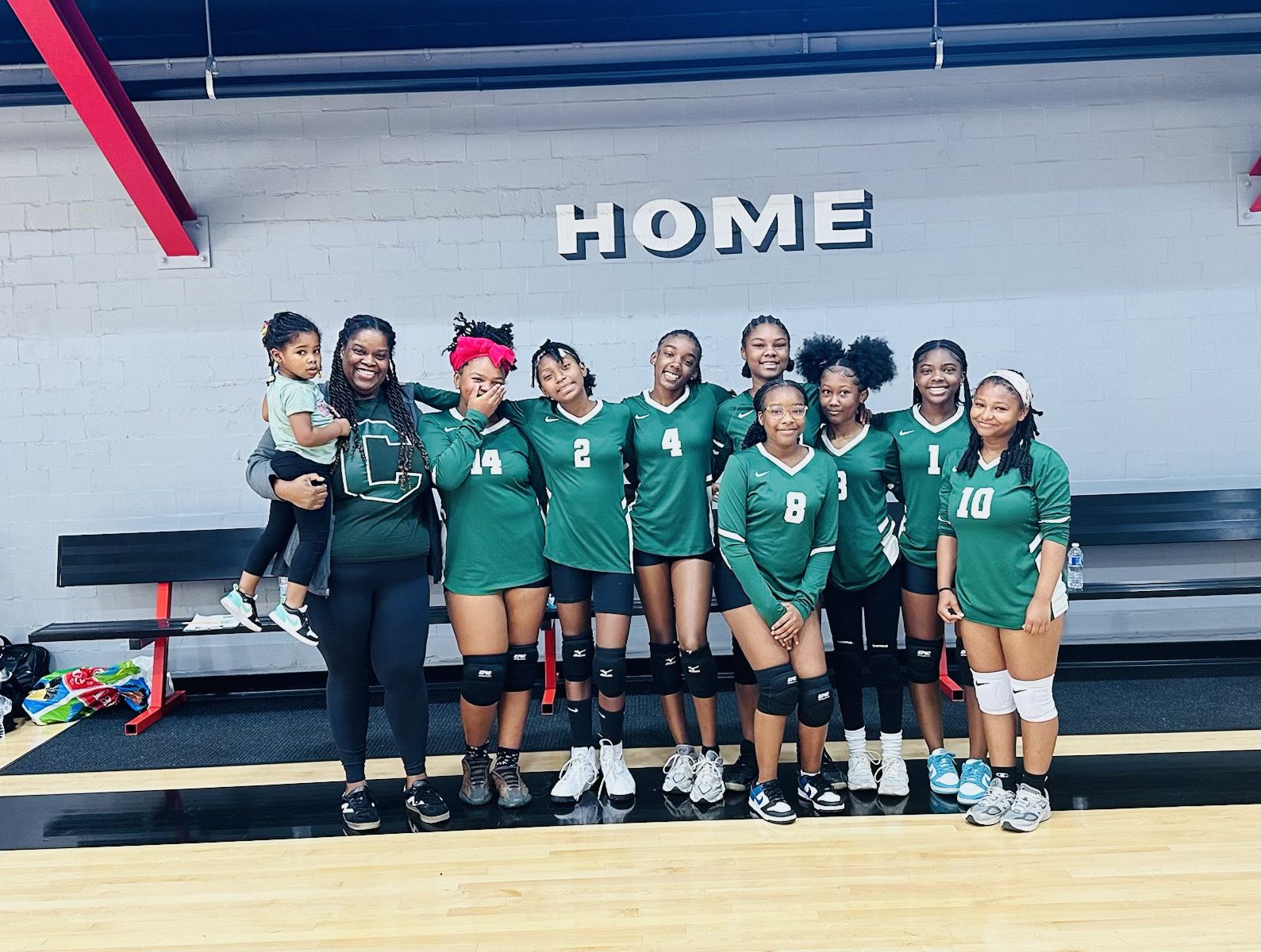 The Comer middle school volleyball team stands in the middle of a gym, posing for a group photo. All the girls are smiling and wearing green and white Comer jerseys.