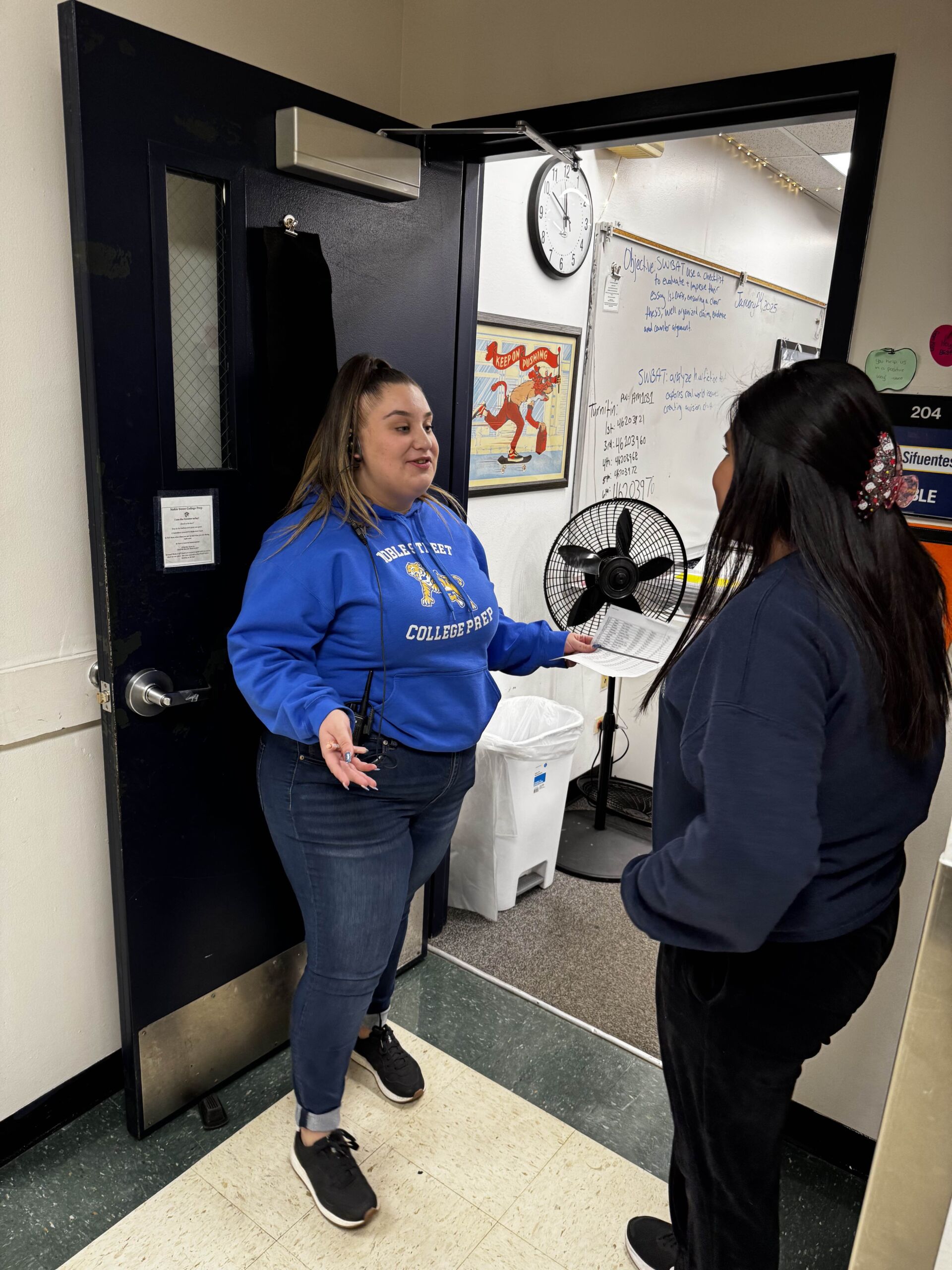 Ms H talks with a student while standing at the door of her classroom.