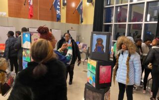 A student poses next to her artwork for a photo in the middle of a crowded art show at Rowe-Clark Math & Science Academy.