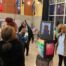 A student poses next to her artwork for a photo in the middle of a crowded art show at Rowe-Clark Math & Science Academy.