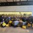 A huge group of Pritzker College Prep girls pose for a photo in McDonalds HQ. They all hold yellow McDonalds goodie tote bags.