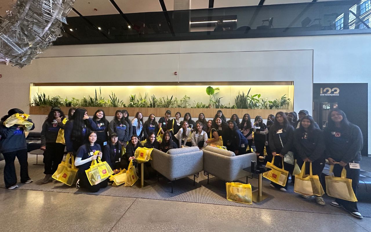 Pritzker Tech World NBA Blog Cover A huge group of Pritzker College Prep girls pose for a photo in McDonalds HQ. They all hold yellow McDonalds goodie tote bags.