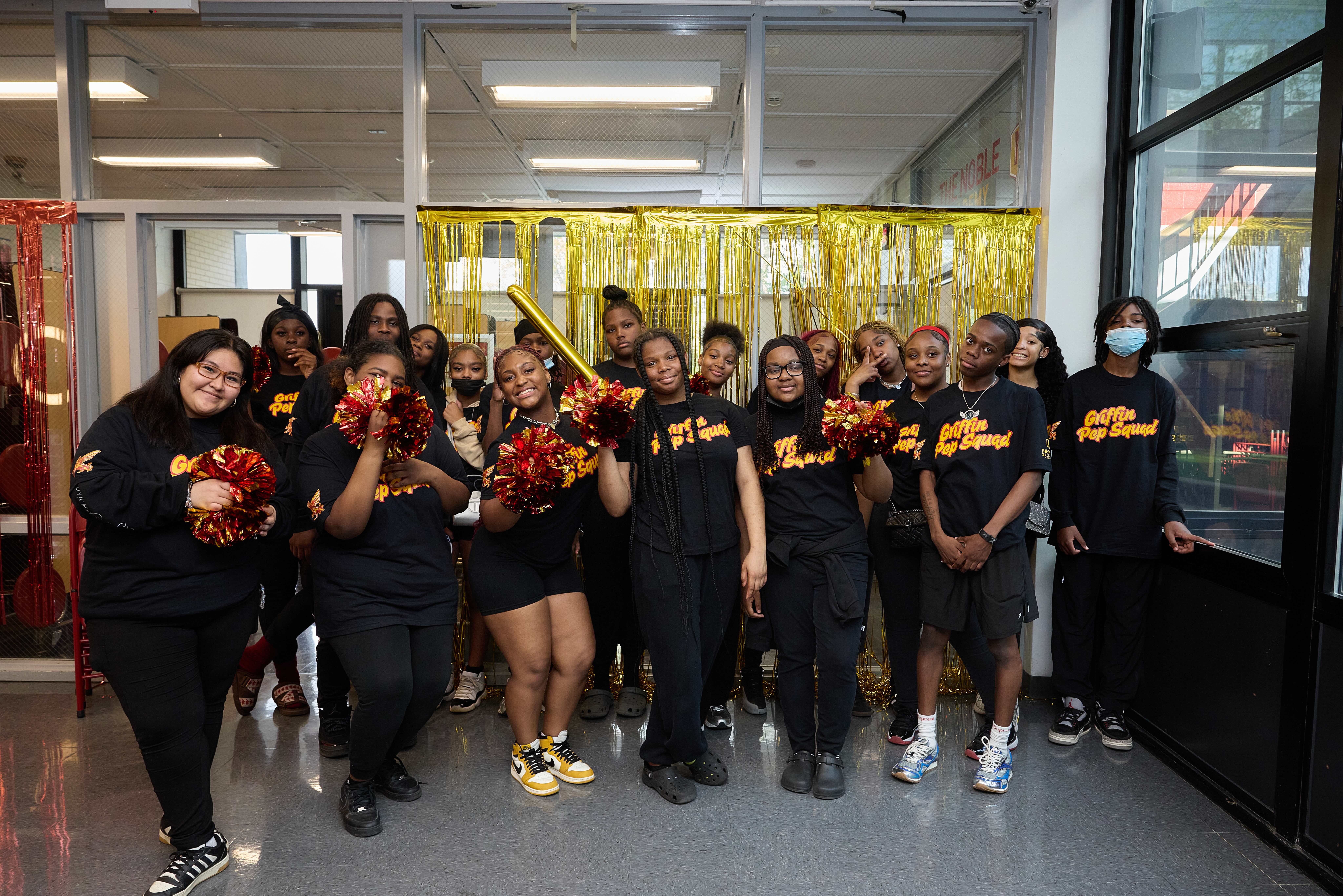 A group of current TNA students who were part of the Pep Squad to welcome incoming freshman pose for a group photo. Many are holding gold and red pom poms.