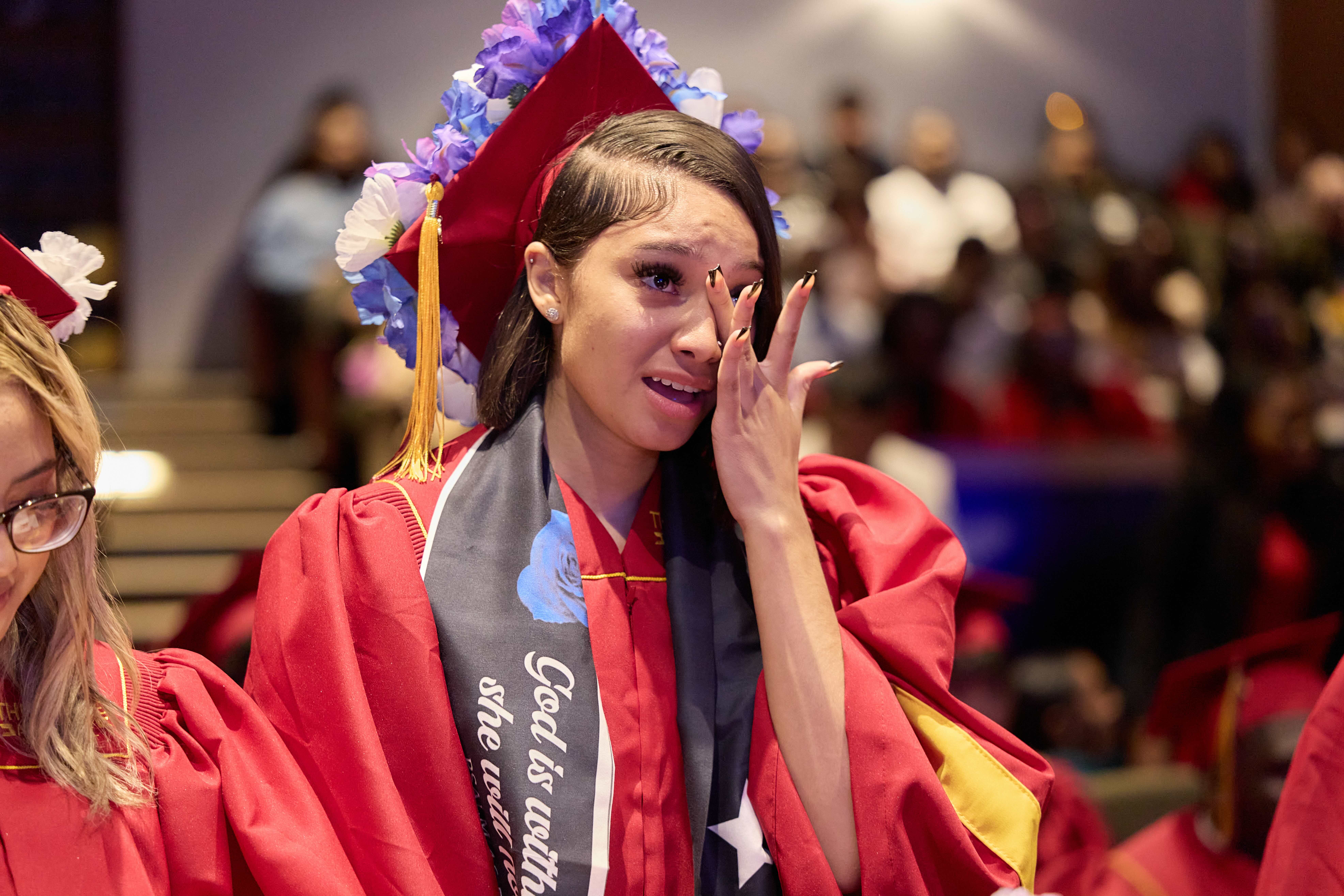 A senior cries at her graduation from TNA. She is blotting away her tears with her hand.