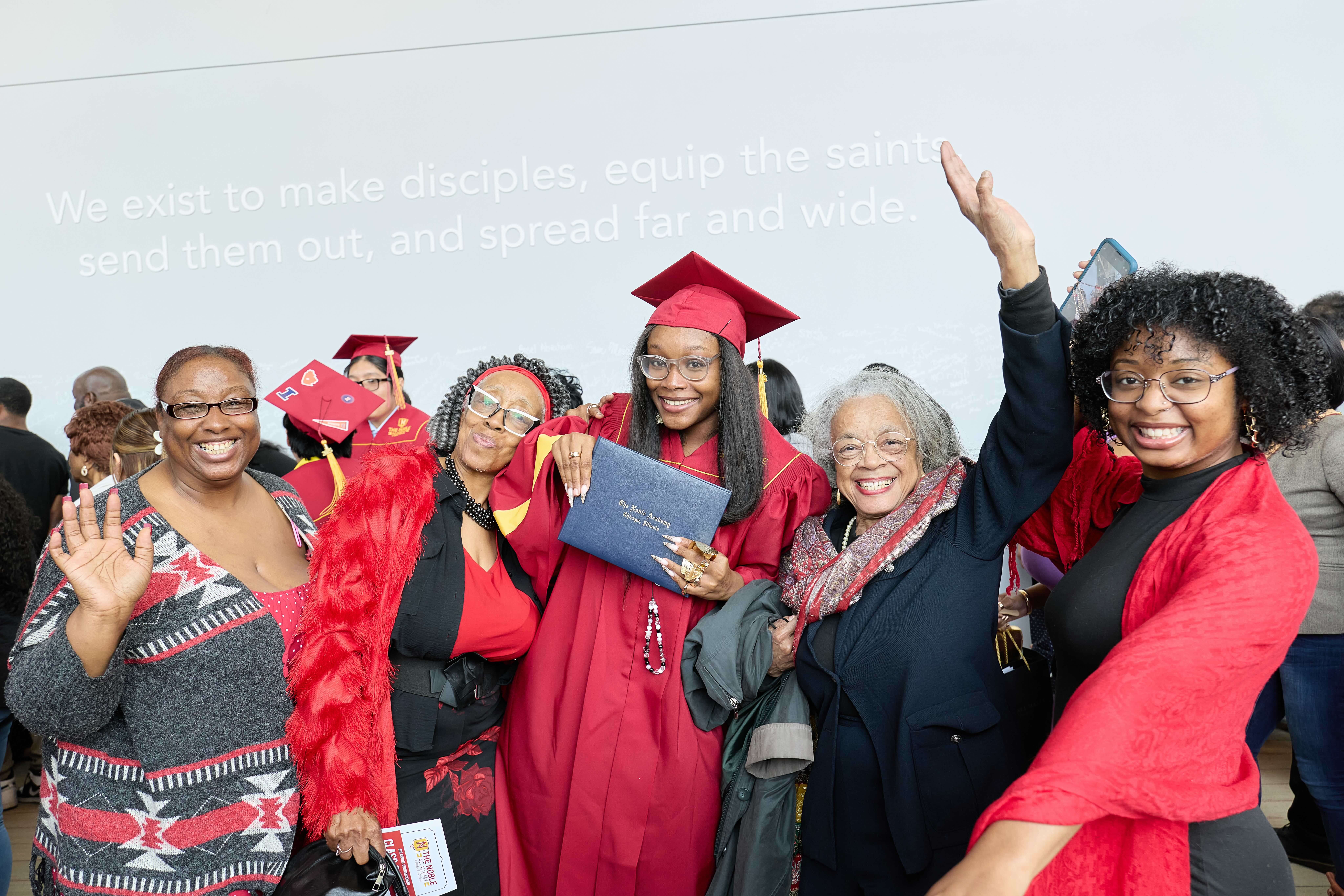 A TNA senior poses with her family after her graduation. They are all smiling and cheering as she holds her diploma.