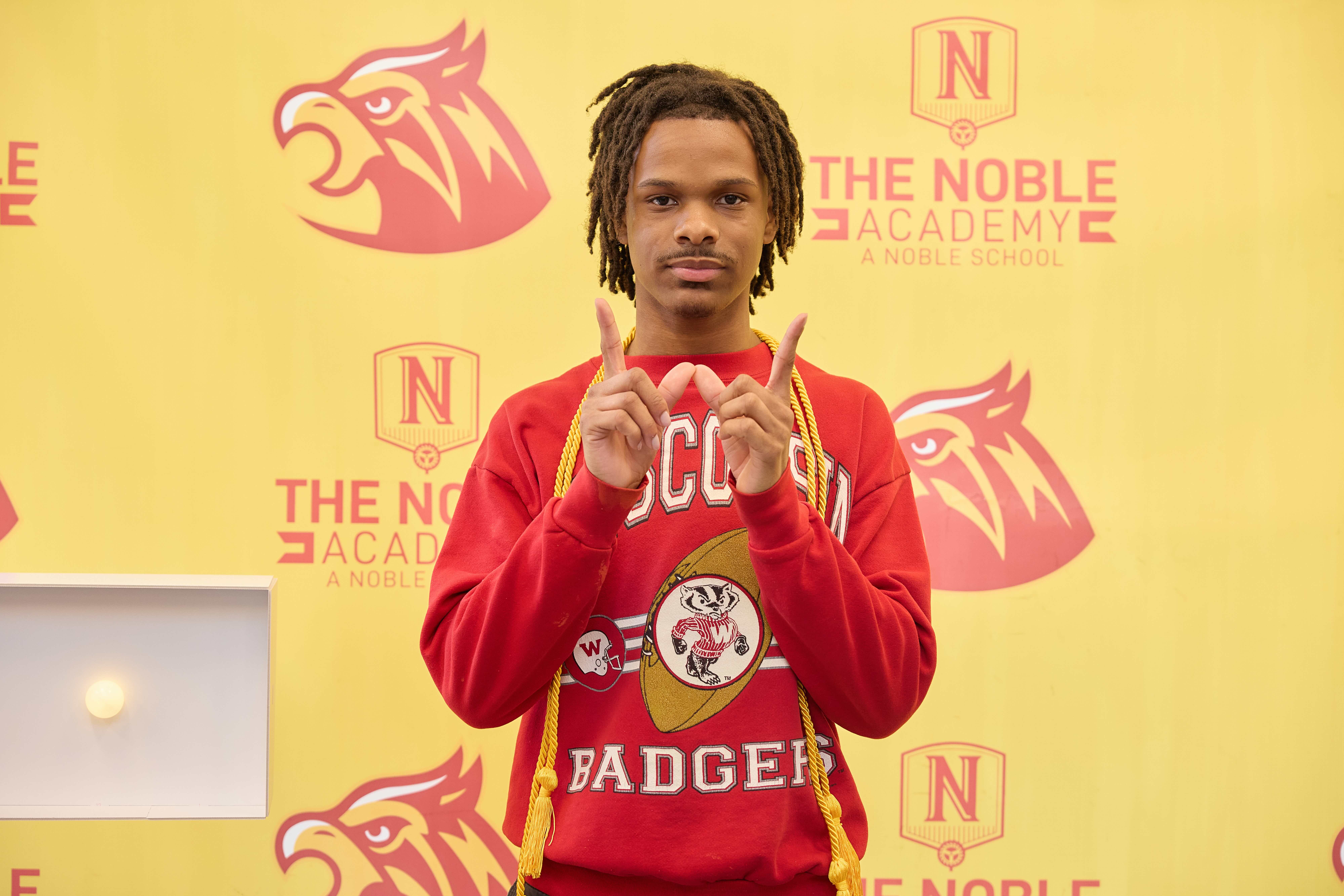 A TNA senior makes a W with his hands while wearing a Wisconsin Badgers sweatshirt. He's going to University of Wisconsin Madison.