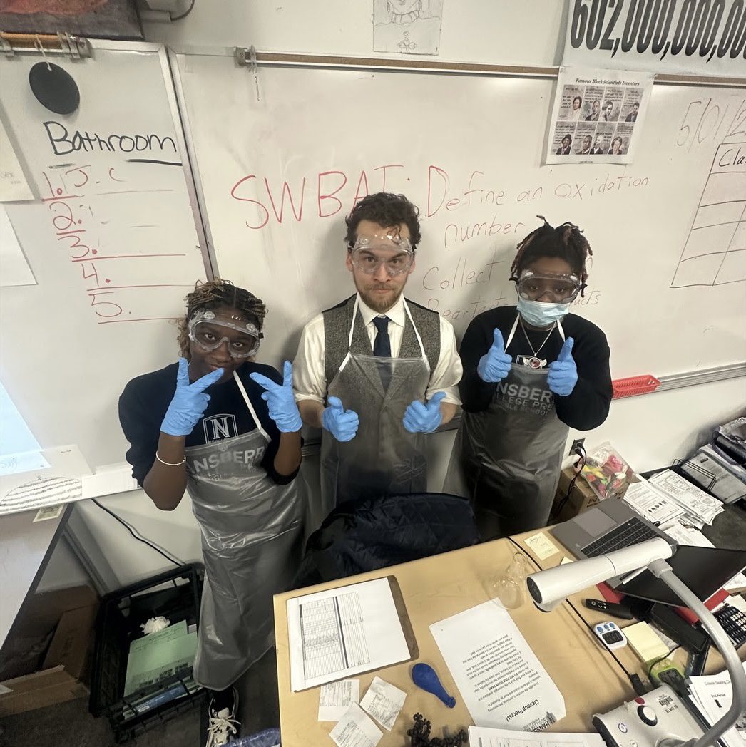 connor celeste hcp Celeste gives two thumbs up next to two of his students in his classroom. They are all wearing protective equipment for a lab. Celeste is a man with short wavy dark brown hair, a full beard, and light skin. Underneath a gray apron, he is wearing a white, long-sleeved button up with a gray vest and black tie.