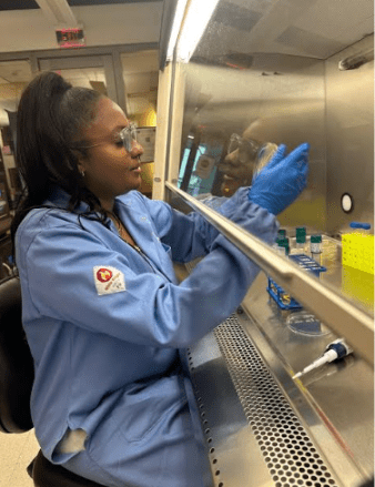 tiffany johnson hcp Johnson holds a some sort of chemical equipment behind a glass shield. She is dressed in light blue protective gear and wears gloves and glasses. She is a woman with long straight black hair in a high ponytail and brown skin.