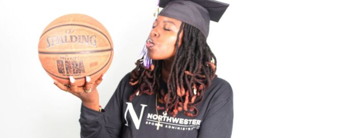 Autumn Jackson, a Gary Comer College Prep alum, holds a basketball and blows a kiss towards it. She is a young Black woman with medium-light brown skin and black locs that flow down past her shoulders and end in a bright burnt orange color. She is wearing a black graduation cap and a black sweatshirt that says "Northwestern Sports Administration" and has the big N Northwestern University logo on it.