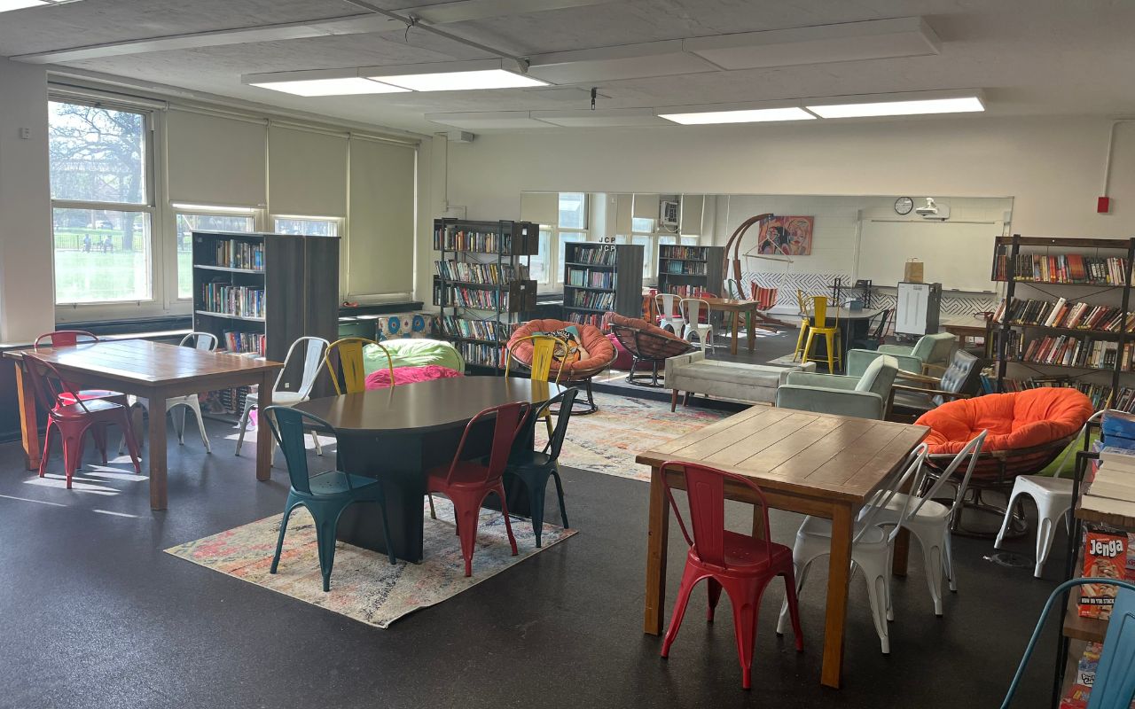 Johnson College Prep's in-house library is full of tables, plush chairs, bean bags, and bookcases. It is well lit and looks cozy with rugs spread out all across the room. A large mirror is on the wall, reflecting most of the spacious library.