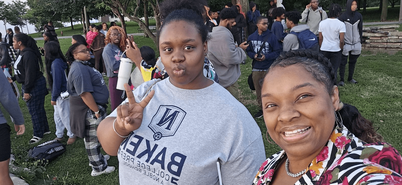 A selfie of Callico-Blackmon with a student. They are outside at a Baker event. You can see a crowd of students and staff behind them. They are both smiling and the student is throwing up a peace sign.
