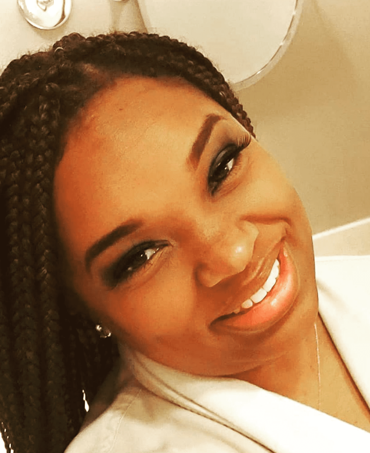 A selfie of Sharon Callico-Blackmon. She is a Black woman with long dark brown braids and medium-light brown skin. SHe is smiling and wearing a white jacket.