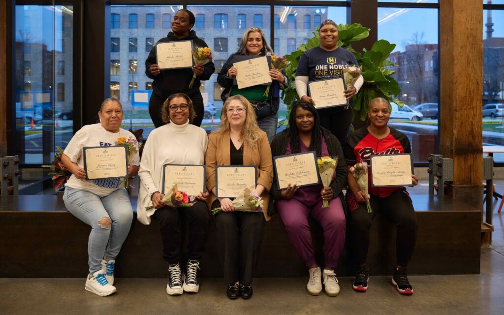 Eight Noble Schools parents stand smiling with their award certificates for completing the Parent Advocacy Training Intensive.