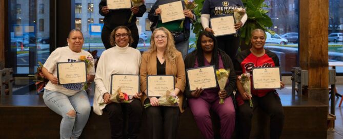 Eight Noble Schools parents stand smiling with their award certificates for completing the Parent Advocacy Training Intensive.
