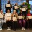 Eight Noble Schools parents stand smiling with their award certificates for completing the Parent Advocacy Training Intensive.