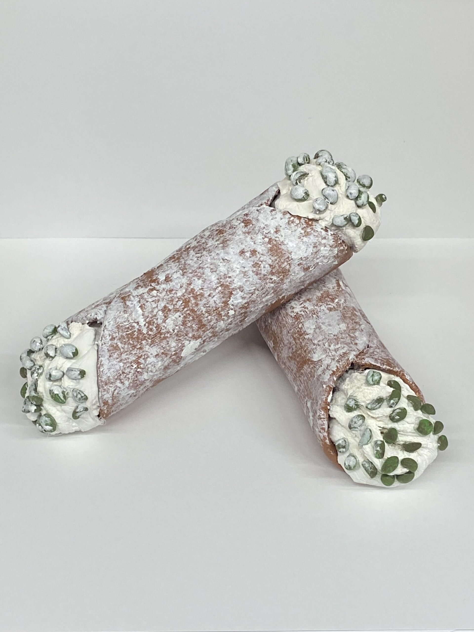 3D 1st Place Cannolis made of clay sit on a blank white background. Brown "sugar-dusted" shells surround white cream studded with green pistachios.
