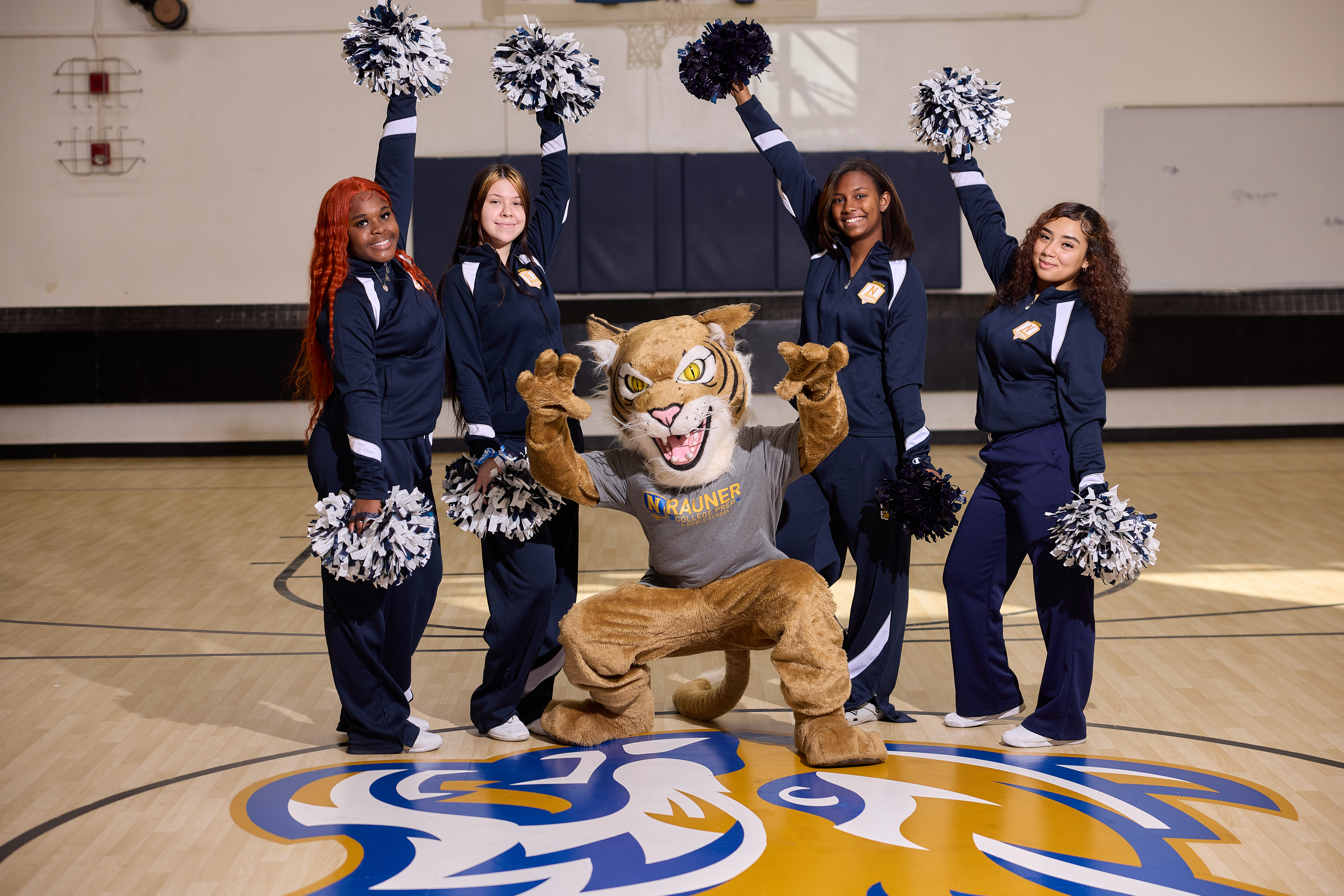 School mascot and cheerleaders smiling and posing in the gym at Rauner College Prep Charter High School in Chicago