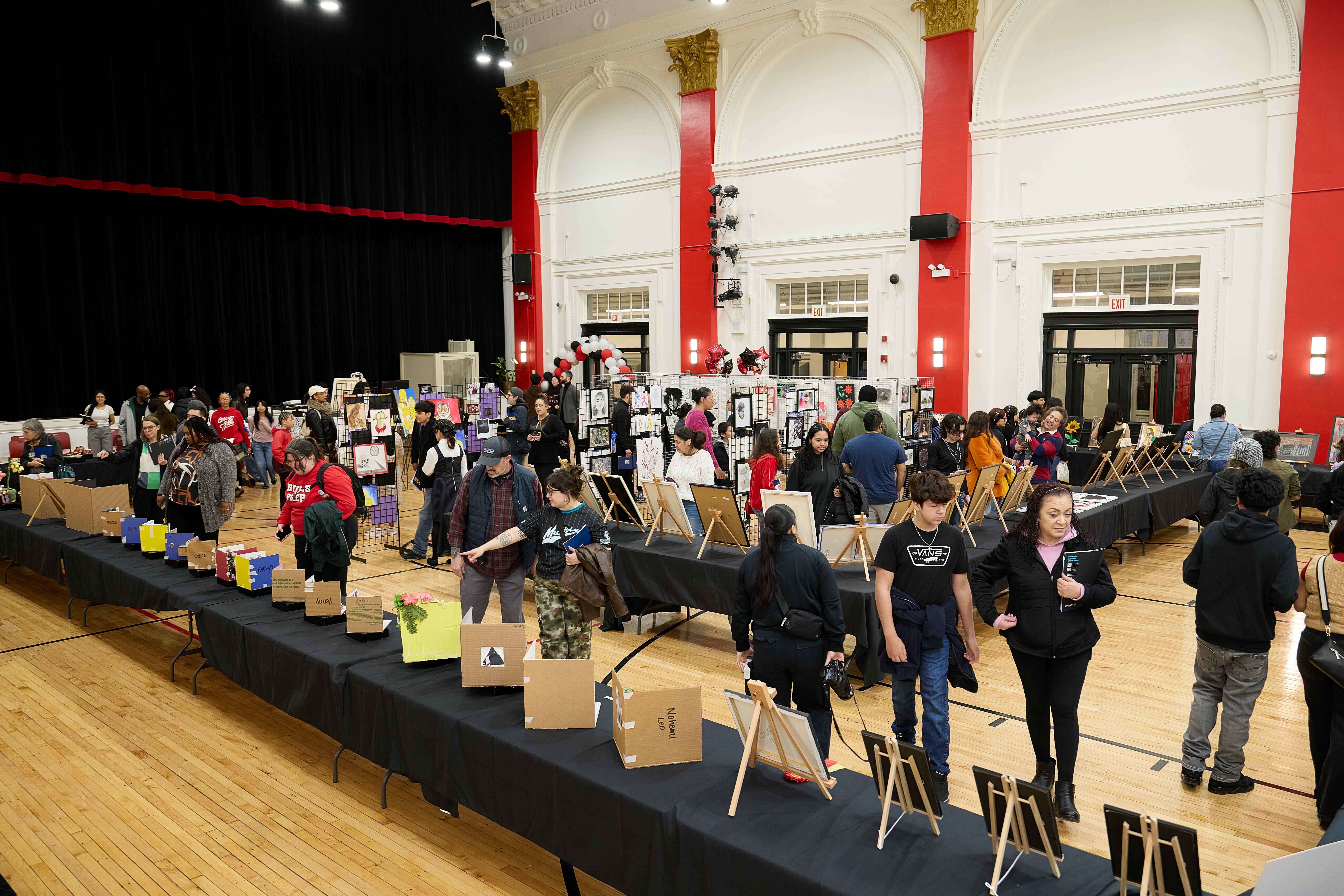 Dozens of people peruse the aisles and tables of the Noble Schools' Visual Arts Festival in 2025. Art lines the tables and are hung up on racks throughout the Chicago Bulls College Prep gym.