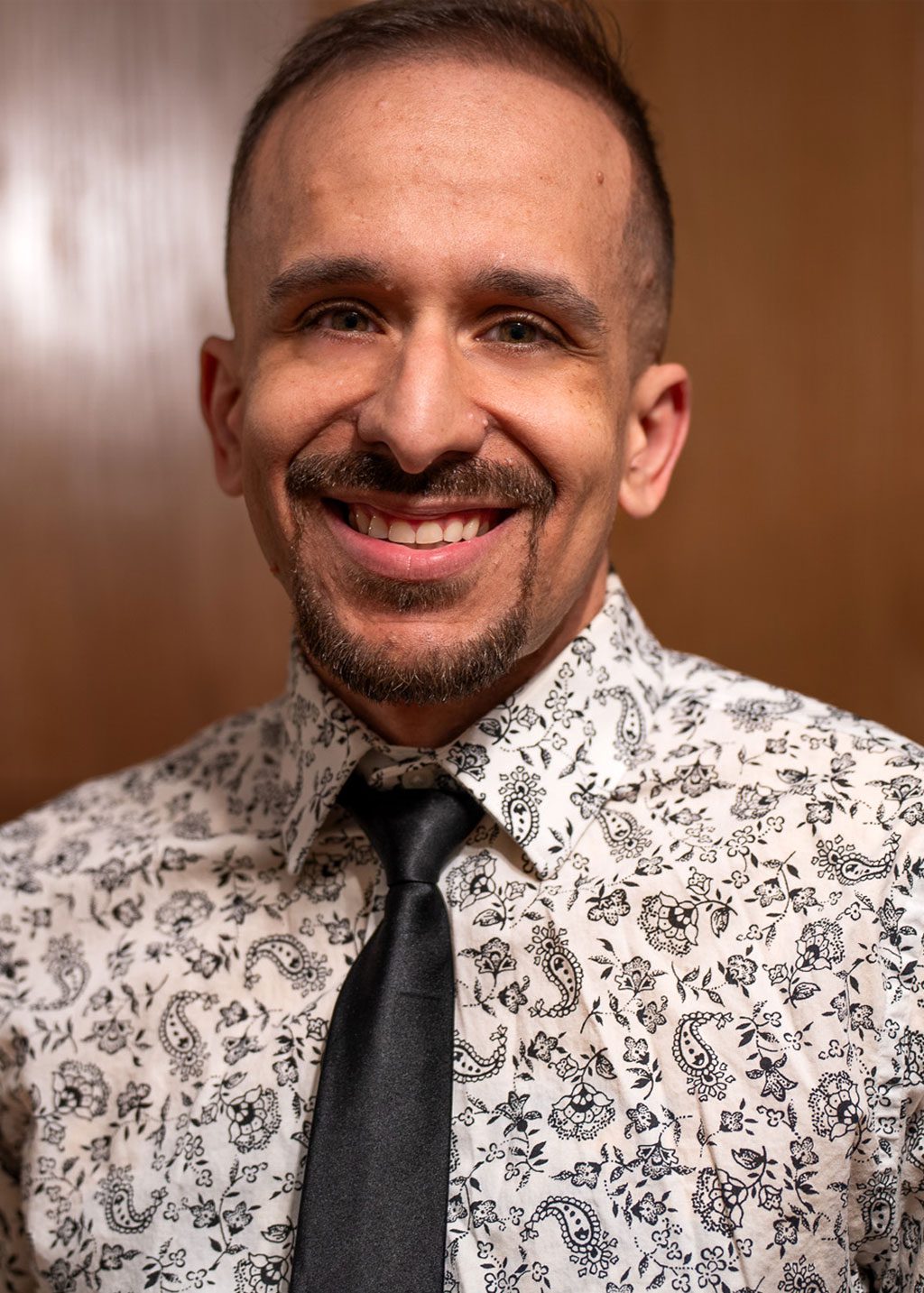Donovan Rosa DLF Cohort 2025 Headshot of Donovan Rosa. He is a Hispanic man, with short fade hair and goatee. He is smiling and wearing a black patterned shirt and black tie.