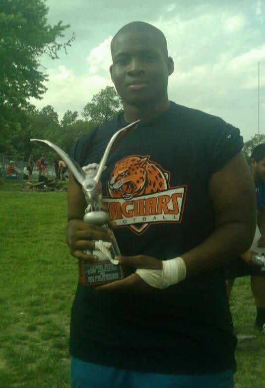 Johnson Student Photo Johnson stands on the rugby field in his jersey, smiling slightly and holding a silver trophy with a big eagle on top.