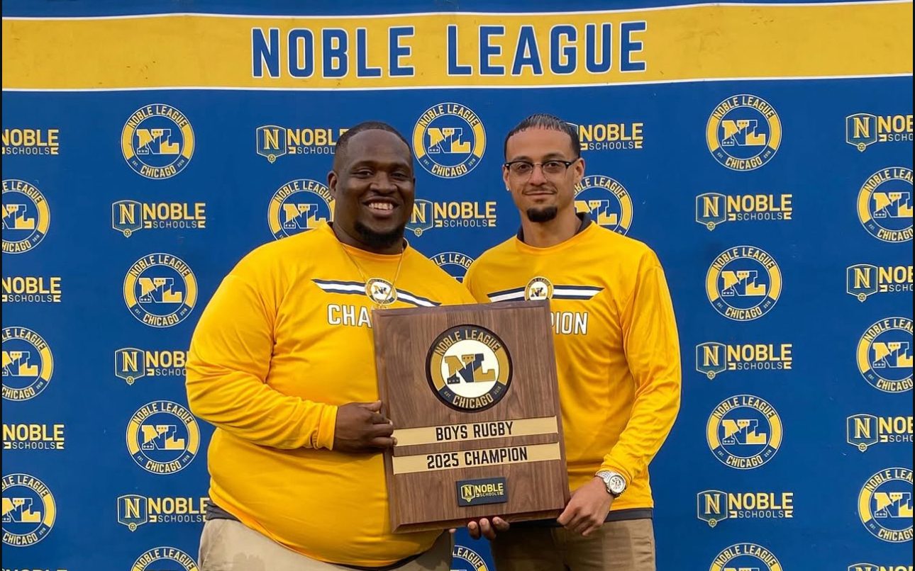 Pritzker College Prep coaches Jovon Hernandez and Anthony Johnson pose for a photo, holding a plaque between them. The plaque says “Boys Rugby 2025 Champions”.
