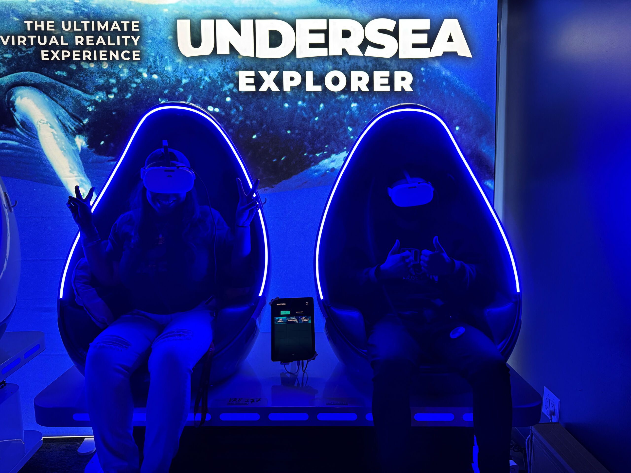 McDonald and her student sit in big glowing blue chairs for the undersea virtual reality experience at the Museum of Science and Industry. They're both wearing bright white VR googles.