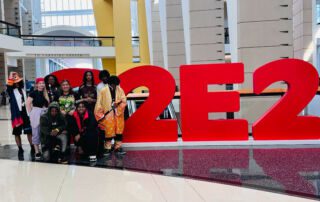 The Baker College Prep esports and anime club stands in front of the giant red C2E2 sign in the big entrance hallway of McCormick Place. They are all dressed up in anime cosplays.