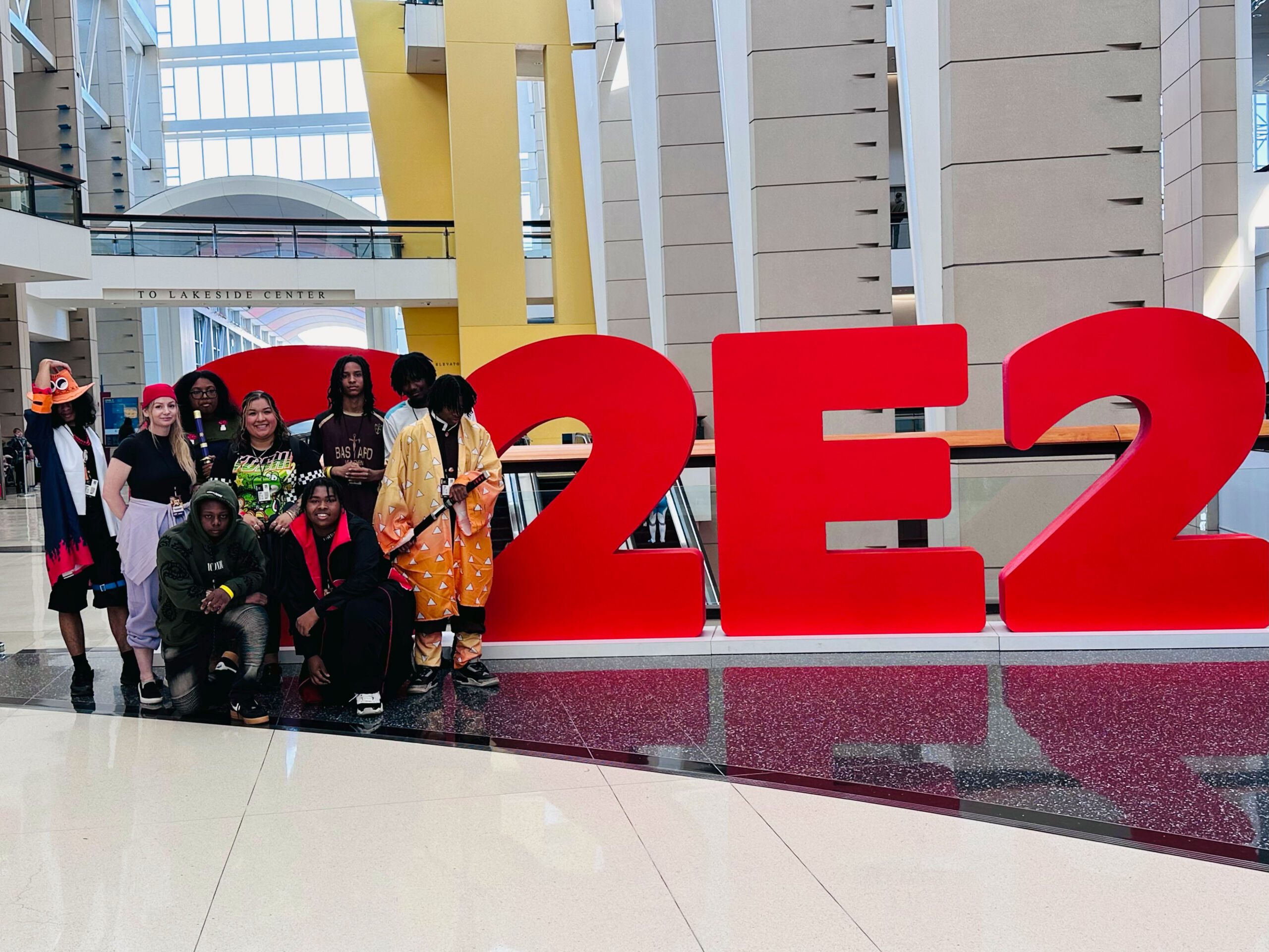 The Baker College Prep esports and anime club stands in front of the giant red C2E2 sign in the big entrance hallway of McCormick Place. They are all dressed up in anime cosplays.