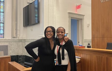 A Noble student stands with an adult professional in what looks like a court room.