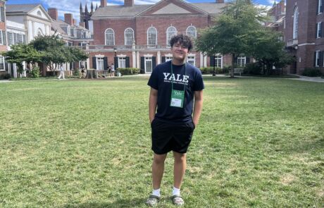 A Noble student stands on the Yale University common area, wearing a t-shirt that says "Yale, Young Global Scholar"