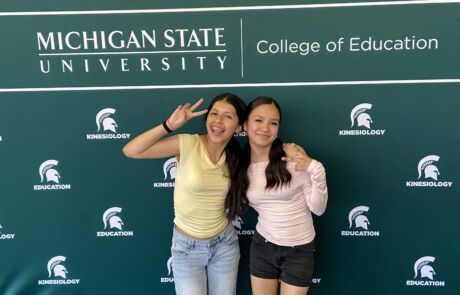 Two students pose in front of a backdrop that says Michigan State University, College of Education.