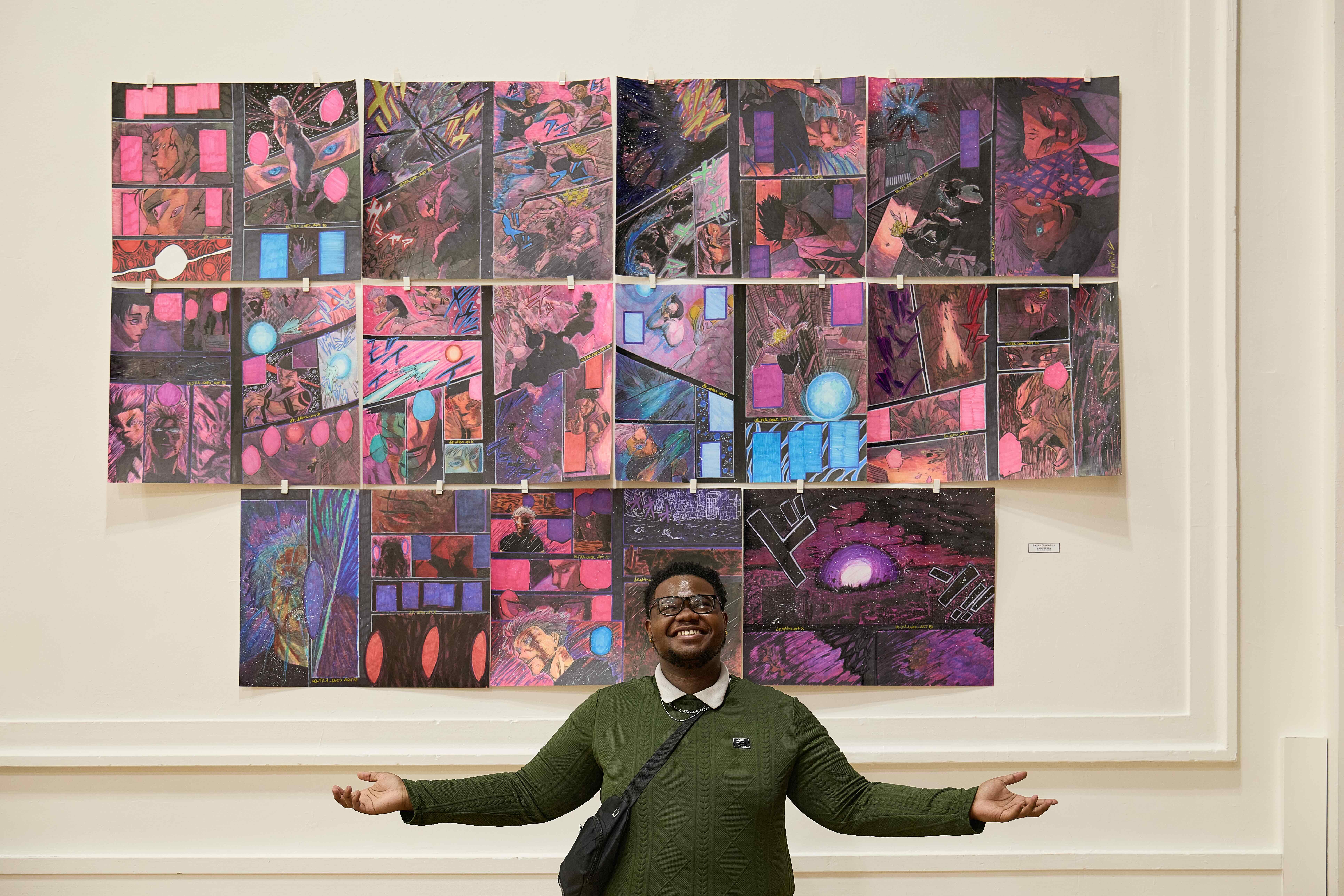 A Hansberry College Prep student stands underneath his massive artwork piece on the wall, his arms splayed out and a smile on his face as he proudly presents it.