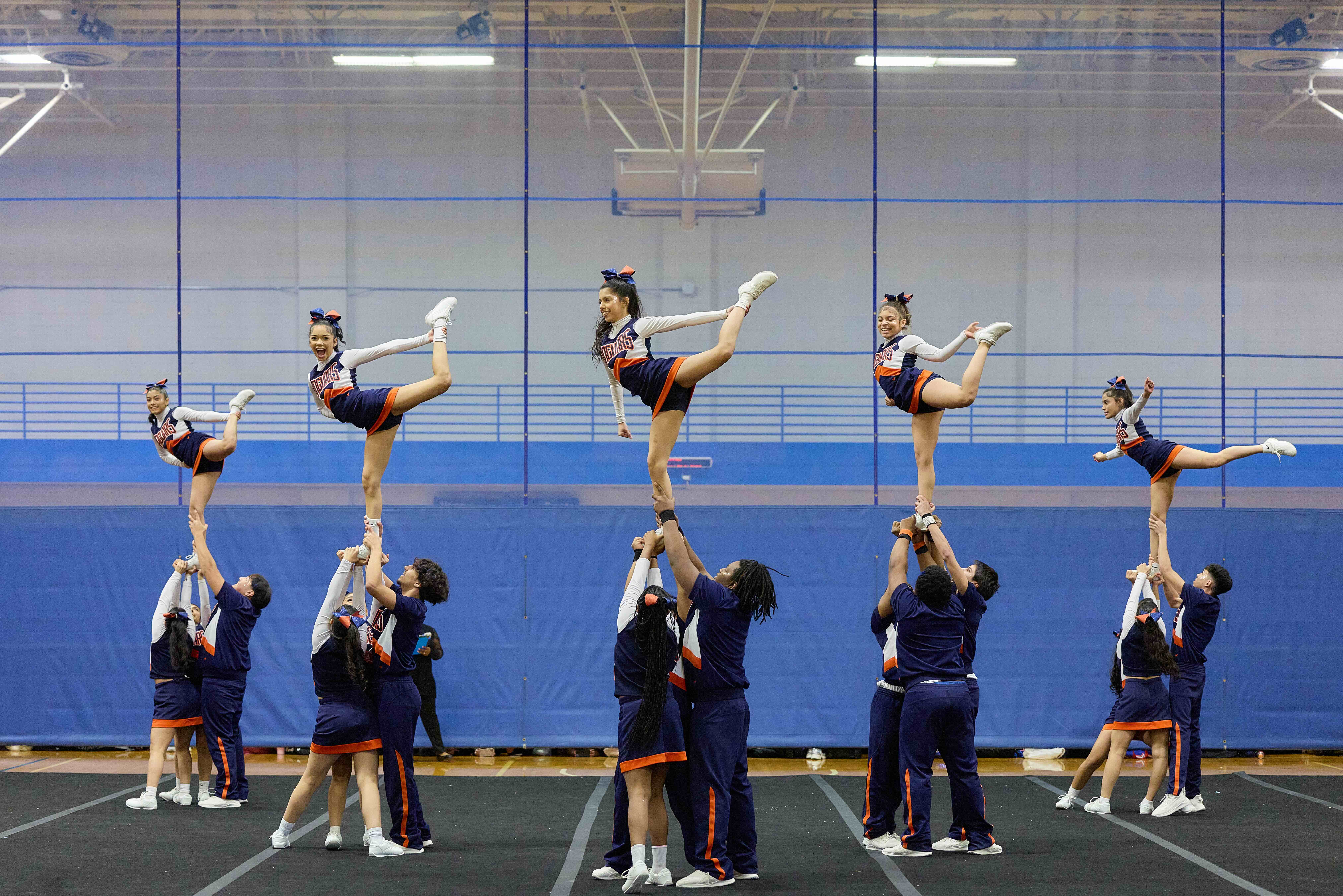 Pritzker College Prep cheerleaders performing, lifting up 5 students who are posing with one leg behind them in the air. They're in a crisp V formation.