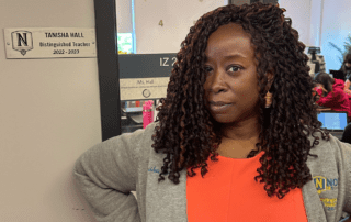 Ta-Tanisha Hall, an African American Literature teacher at ITW David Speer Academy in Chicago, IL, stands at the door to her classroom. She is smiling confidently and standing next to the plaque on the side of her door that says "Tanisha Hall, Distinguished Teacher, 2022-2023"