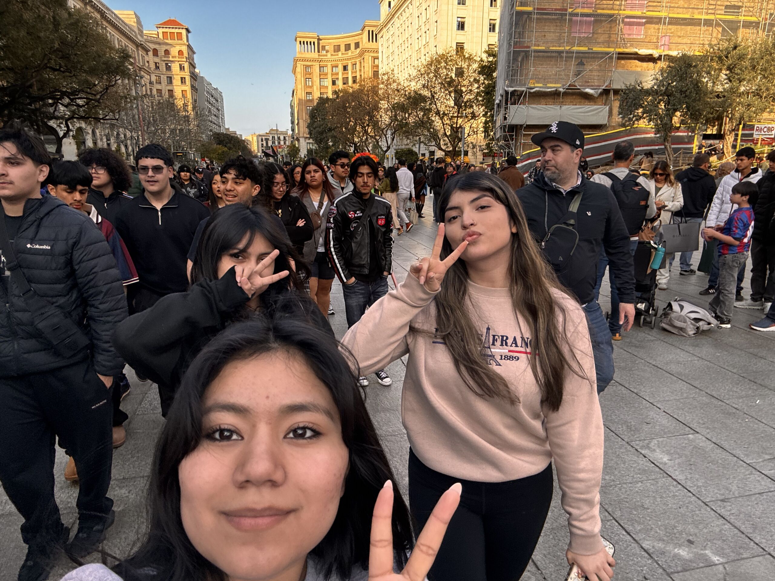 untitled (4) Belinda, Elleney and another Mansueto student take a selfie while walking down the streets of Barcelona with the whole group. They're all putting up peace signs.