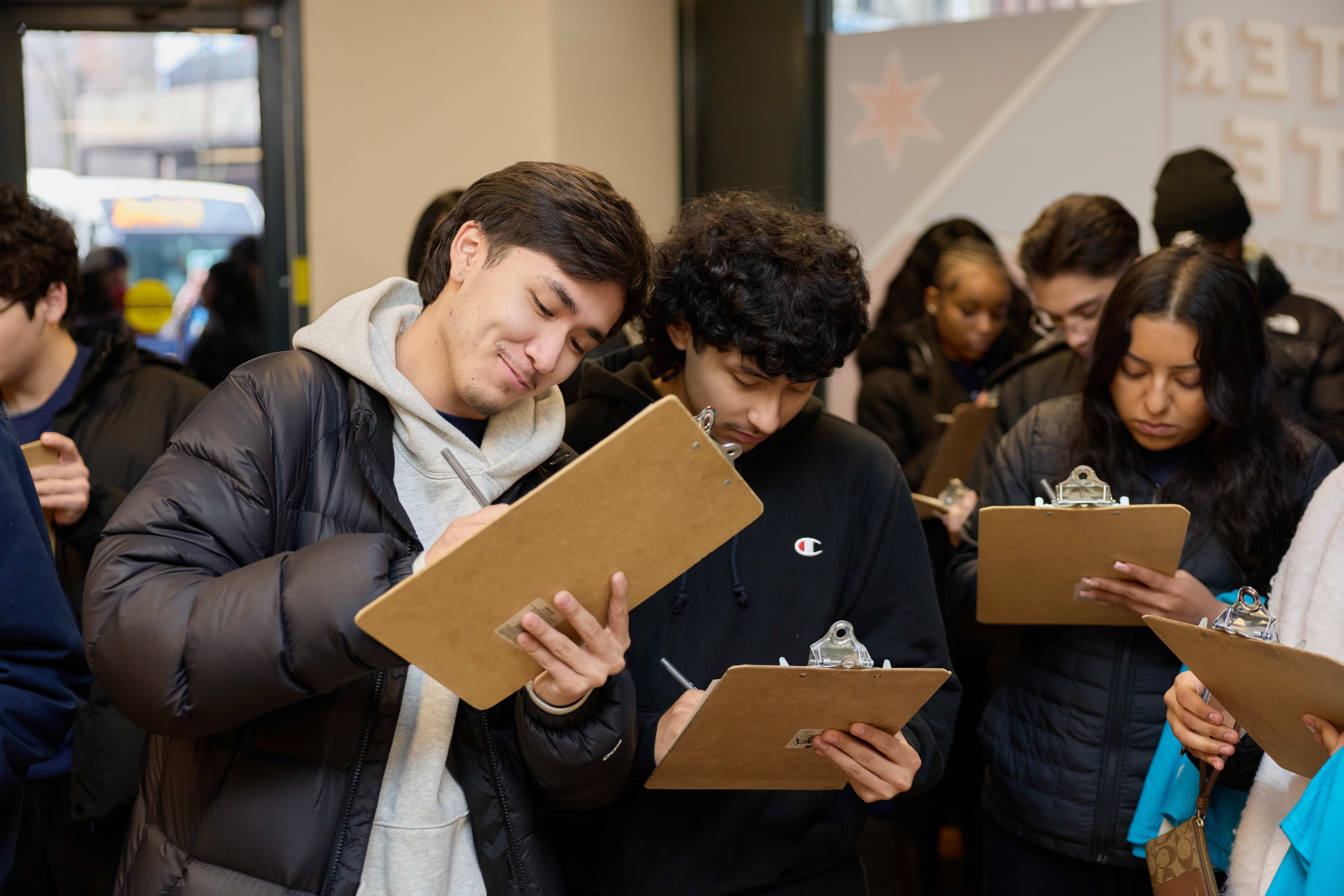Multiple Noble students stand inside the voting site, writing on clipboards.
