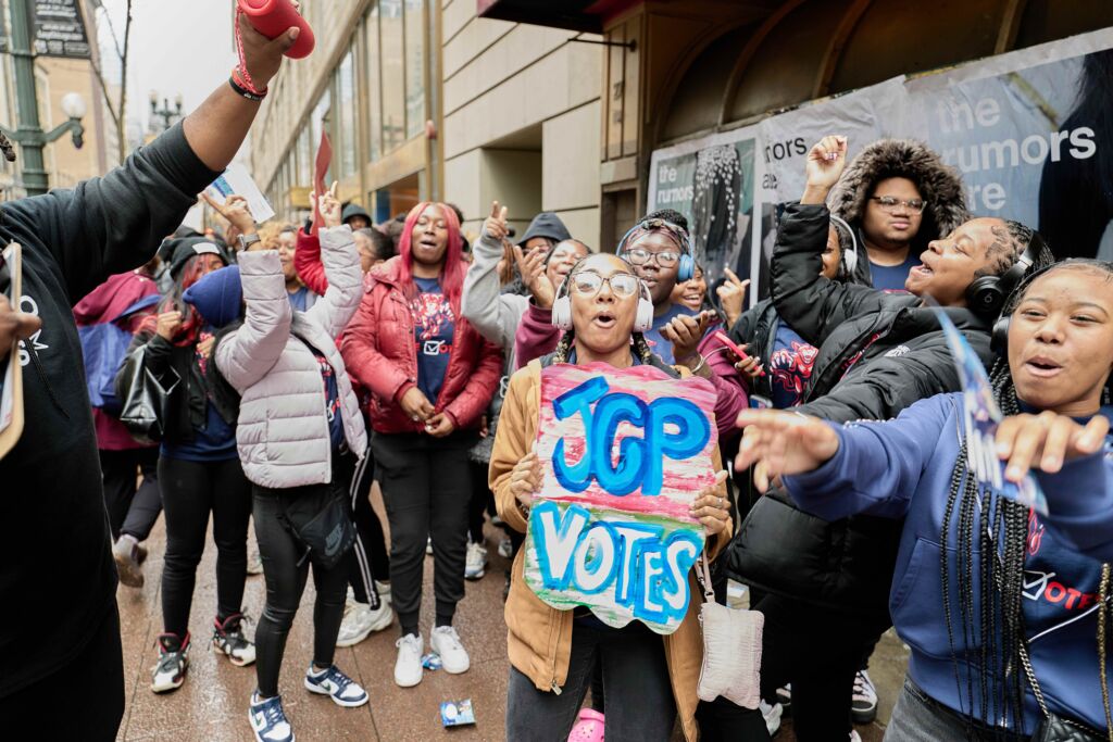 A Johnson College Prep student holds a colorful sign that says "JCP Votes". She is surrounded by her peers and they all seem to be cheering and chanting. The excitement for these Chicago high school students to vote for the first time is clear in this scene.