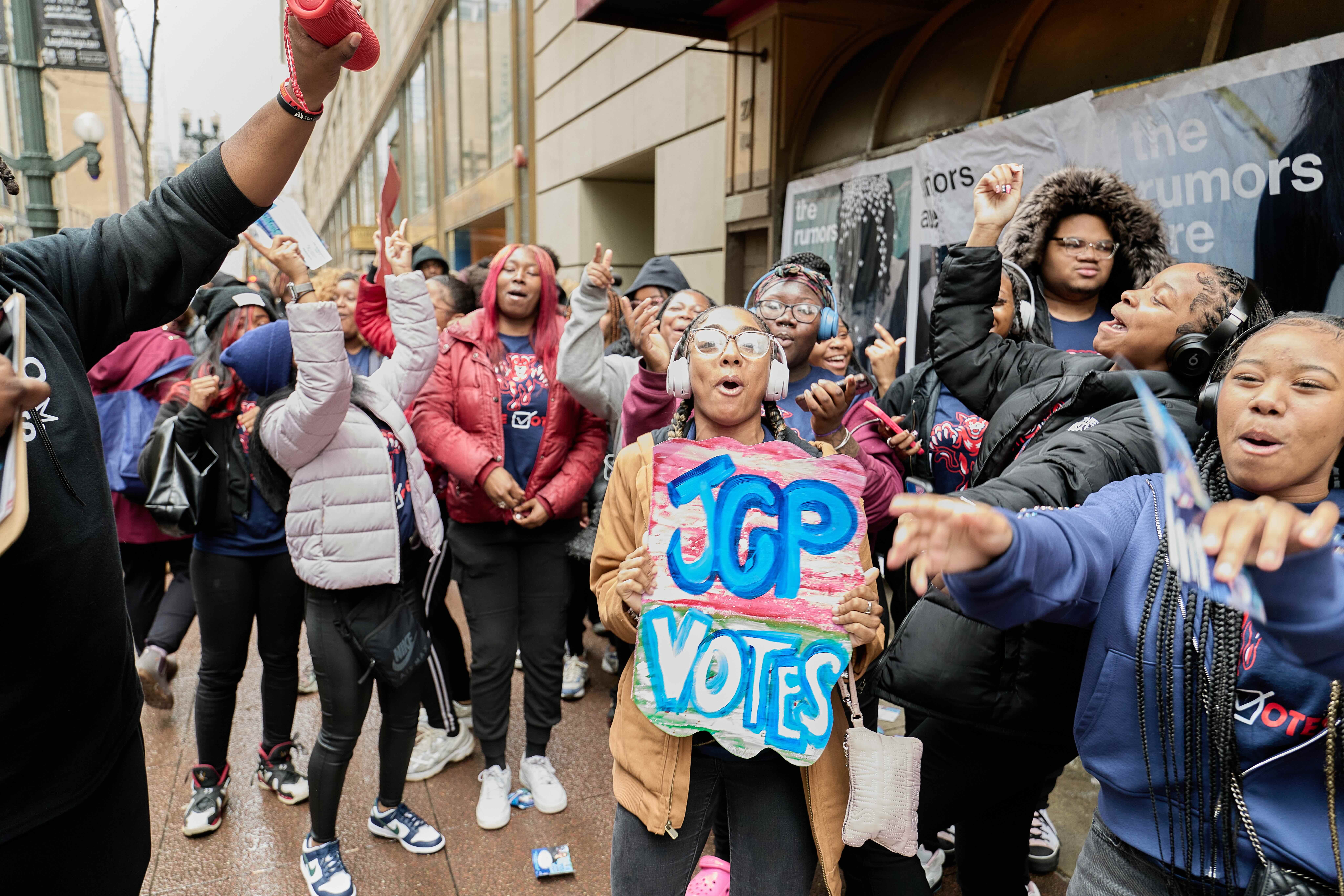 A Johnson College Prep student holds a colorful sign that says "JCP Votes". She is surrounded by her peers and they all seem to be cheering and chanting. The excitement for these Chicago high school students to vote for the first time is clear in this scene.